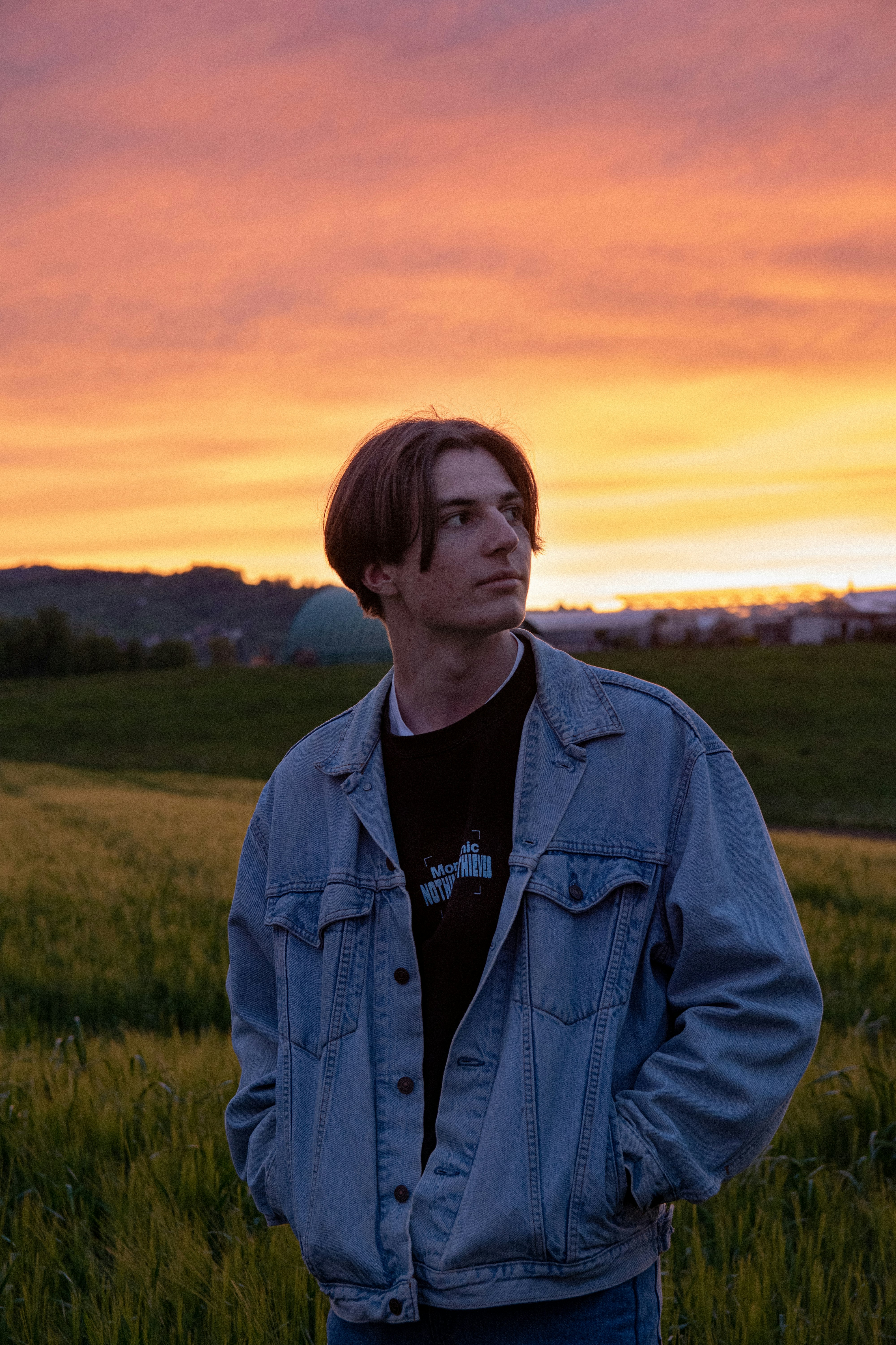 man in blue denim jacket standing on green grass field during sunset